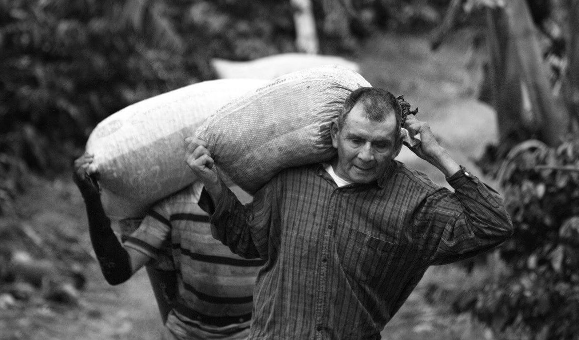Fotografía tomada en blanco y negro, de un señor cargando un bulto de papa